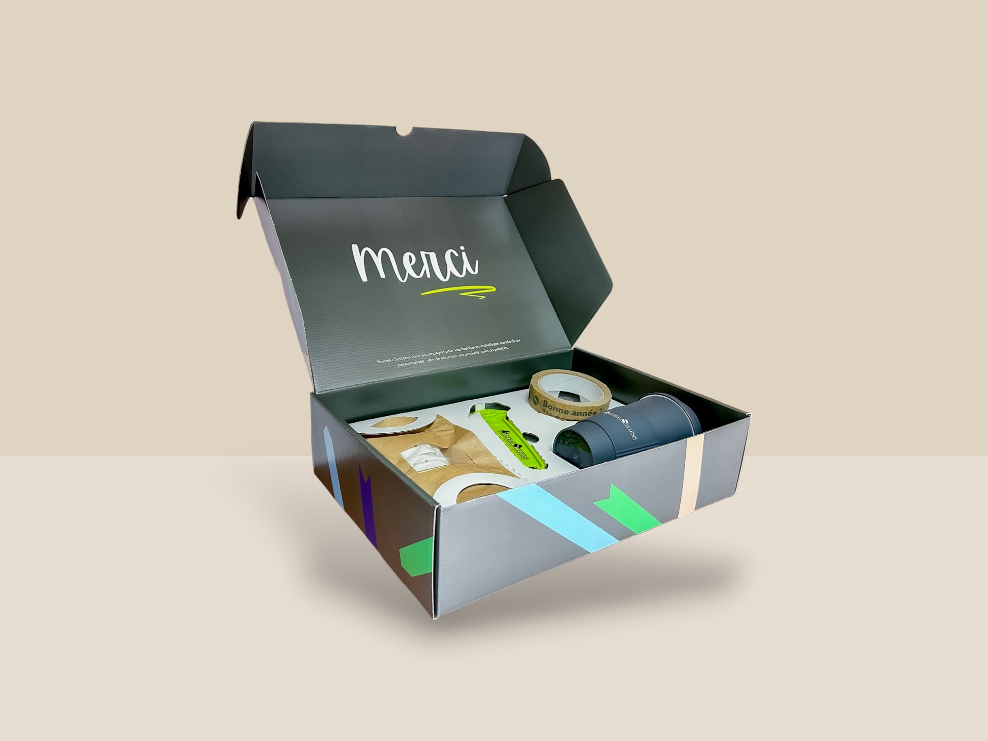 Une boite verte, ouverte avec des articles à l'intérieur, scotch, cutter et gobelet.