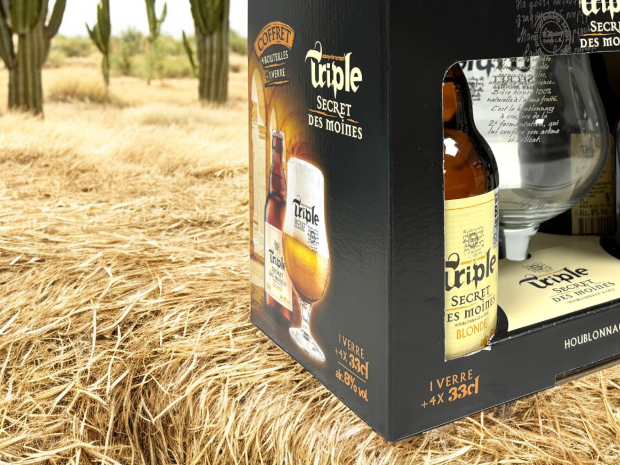 Un coffret triple secret des moines destinée à contenir des bouteilles de bière et des verres. Le packaging est posé sur un ballot de paille. Il est de couleur noire, marron et beige.