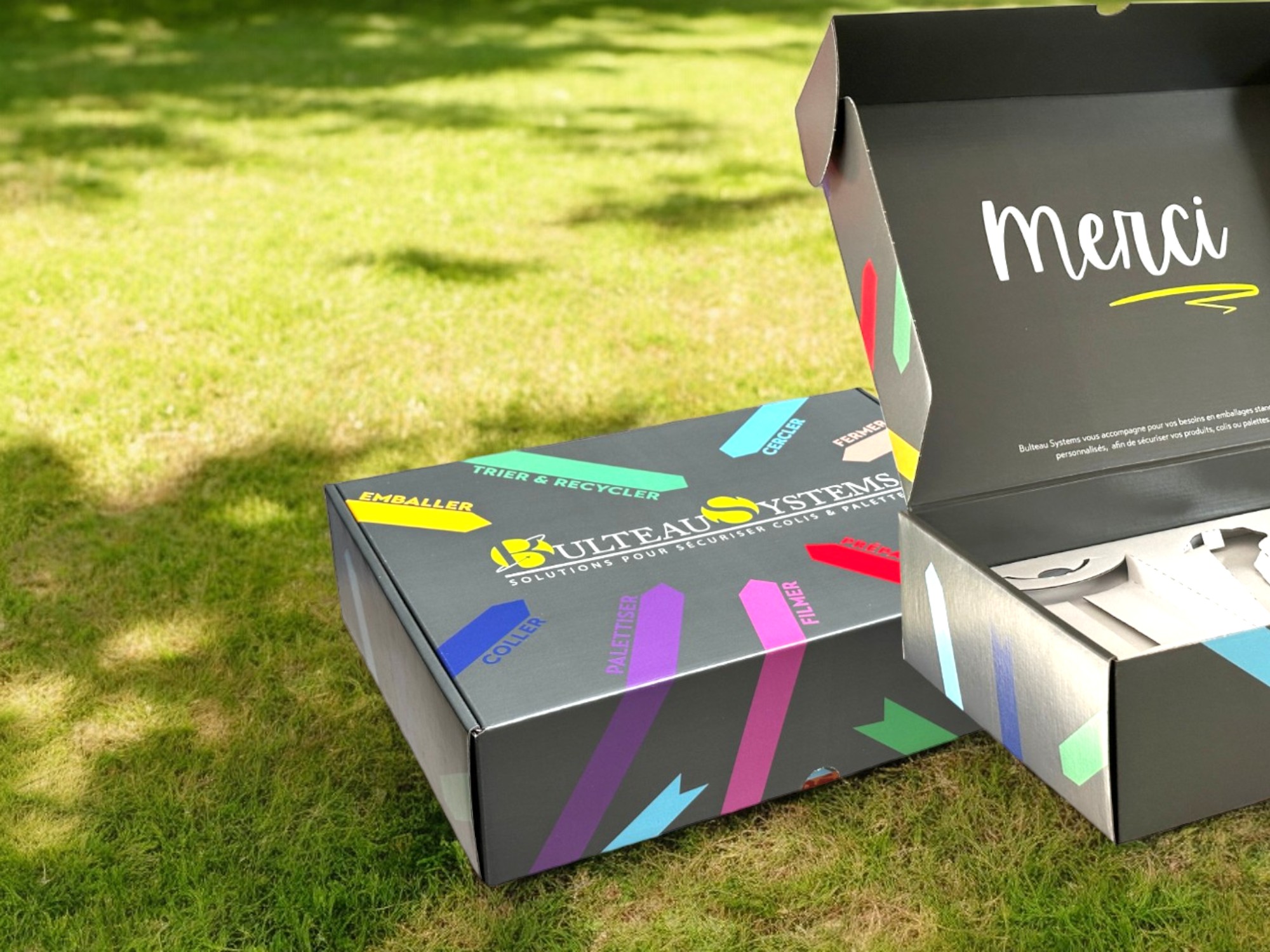 Une boite verte, ouverte avec des articles à l'intérieur, scotch, cutter et gobelet.